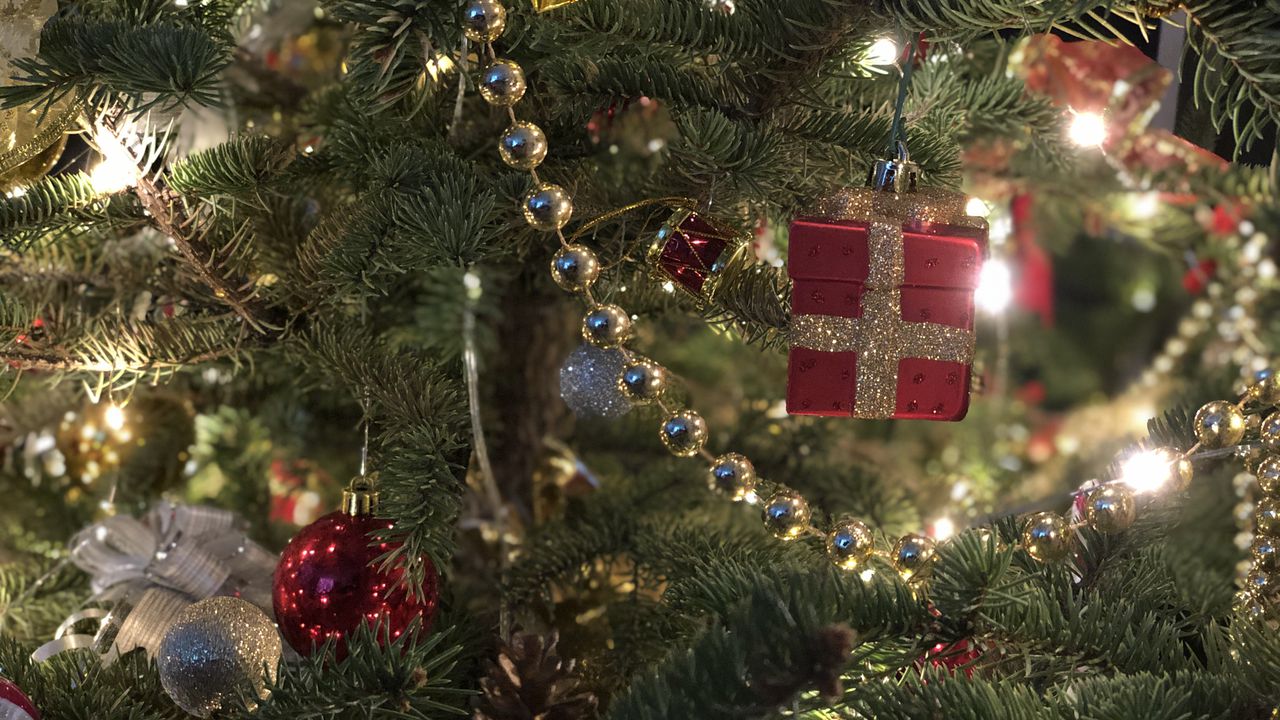 Крупний план новорічної ялинки, прикрашеної святковими золотими намистами, червоними іграшками-подарунками та теплими вогниками, що створює атмосферу магії Нового року.