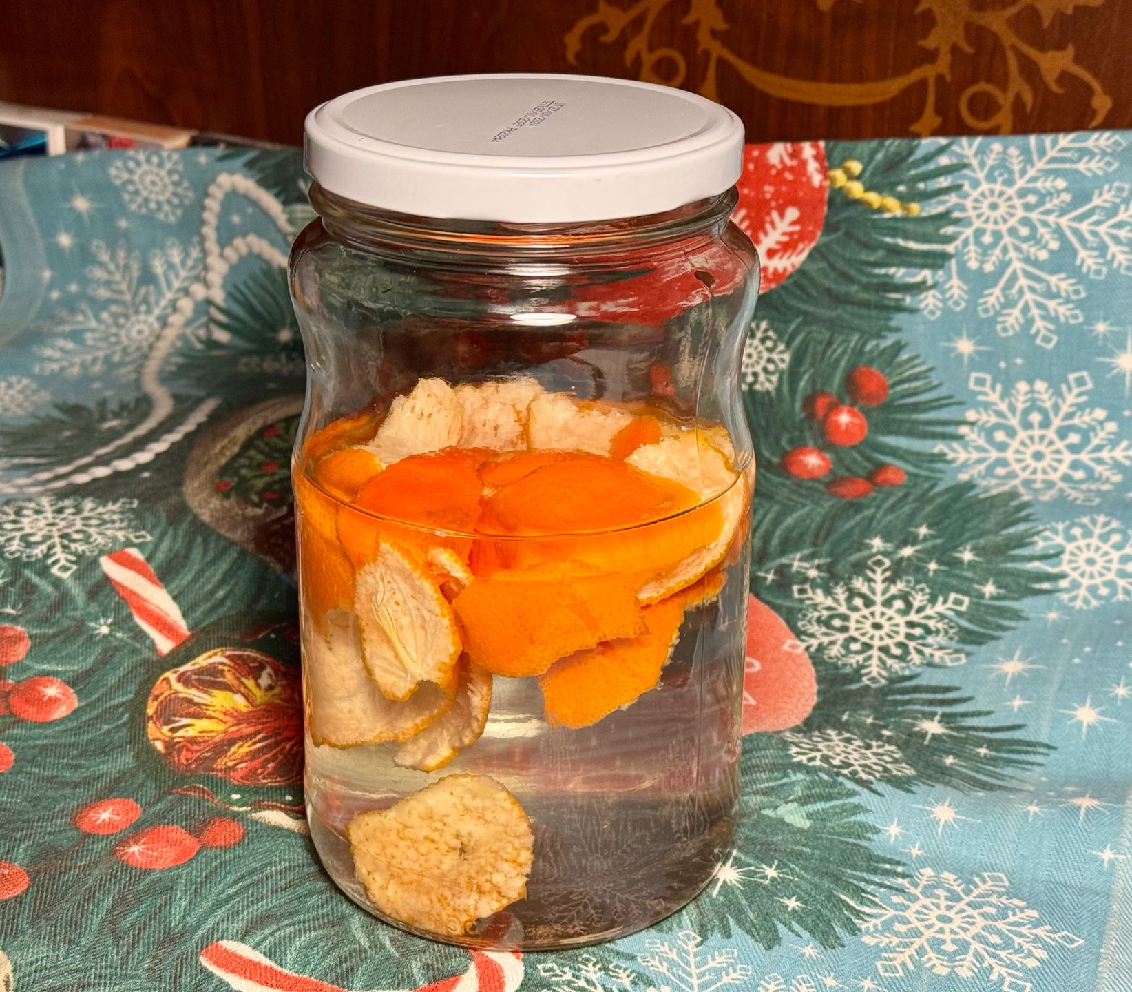 Скляна банка з мандариновими шкірками для приготування ароматної домашньої настоянки або мандаринової горілки на новорічному столі.