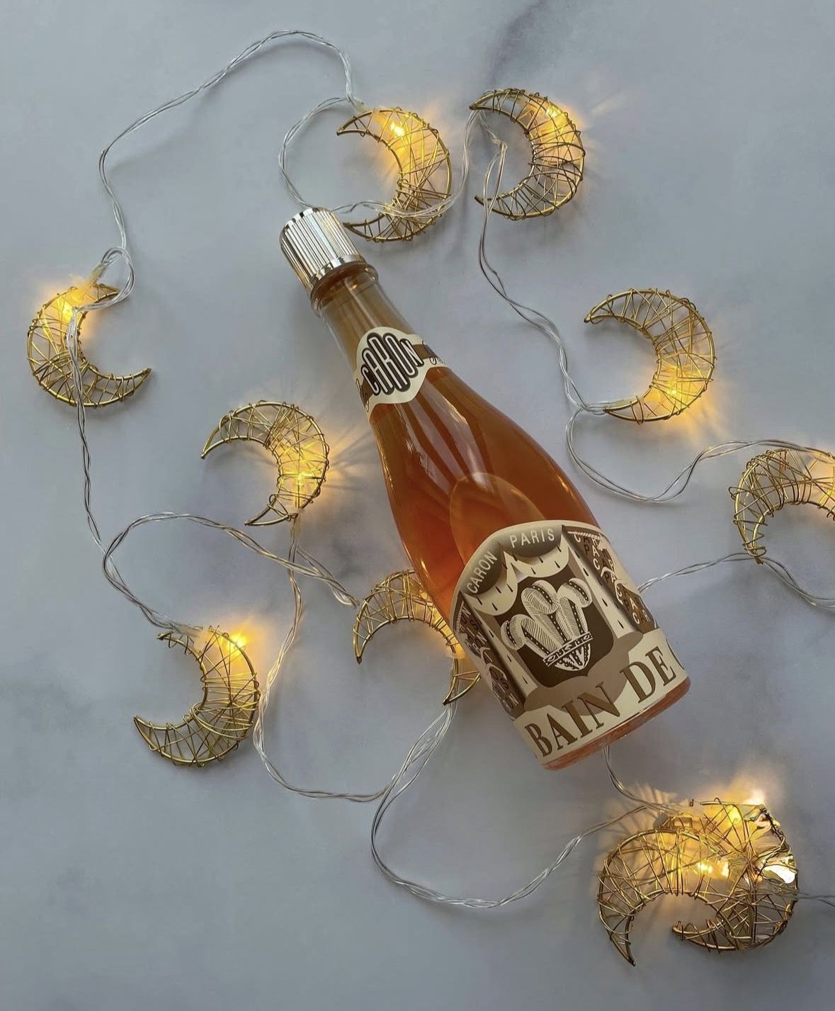 Парфуми Caron Paris Bain de Champagne у святковій атмосфері з золотою новорічною гірляндою