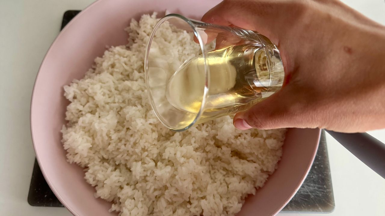 Процес приготування рису для суші — додавання оцтової заправки у варений білий рис у мисці.