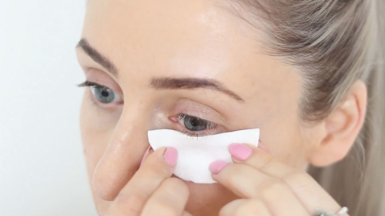 Процес підготовки до фарбування вій вдома: захист шкіри під очима за допомогою ватного диска перед процедурою.