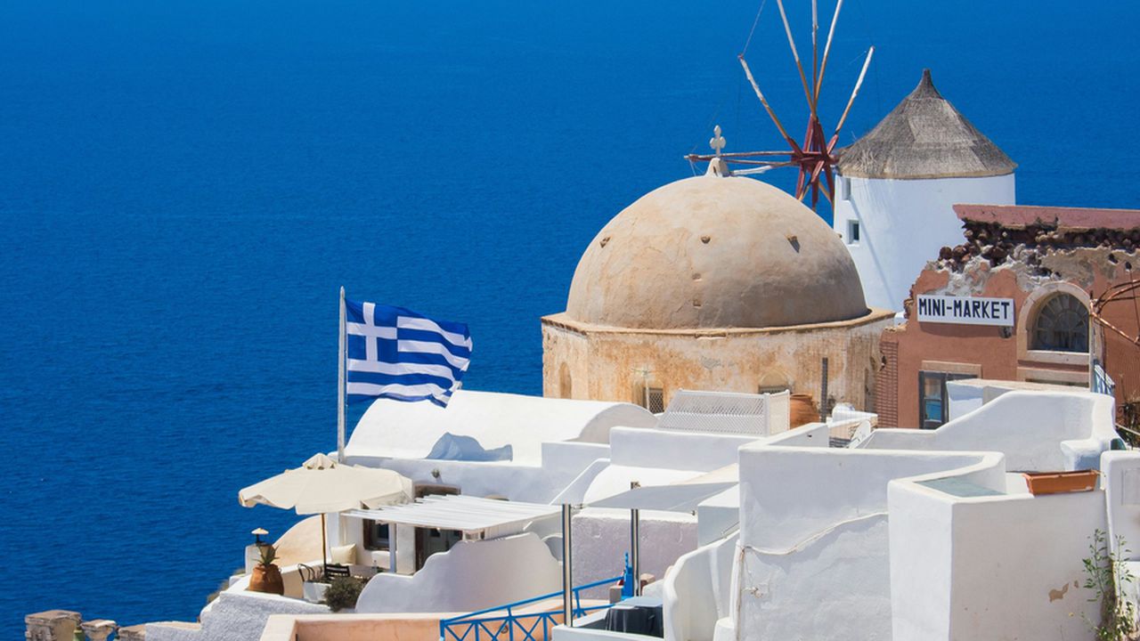 Краєвид Греції (Еллади): національний грецький прапор на фоні білих будинків, традиційного млина та синього моря.
