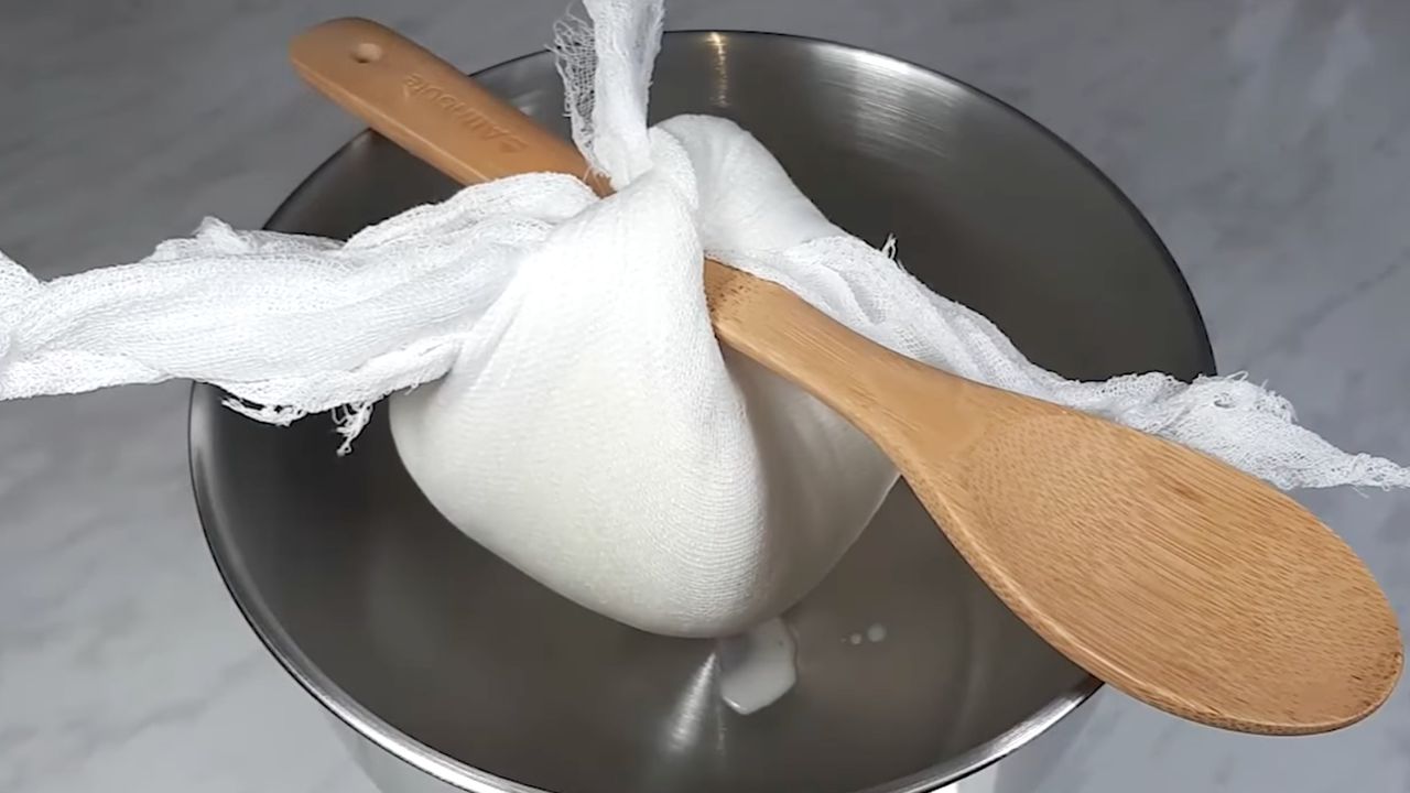 Процес відціджування сметани через марлю для приготування густого та шовковистого сметанного крему для медовика.