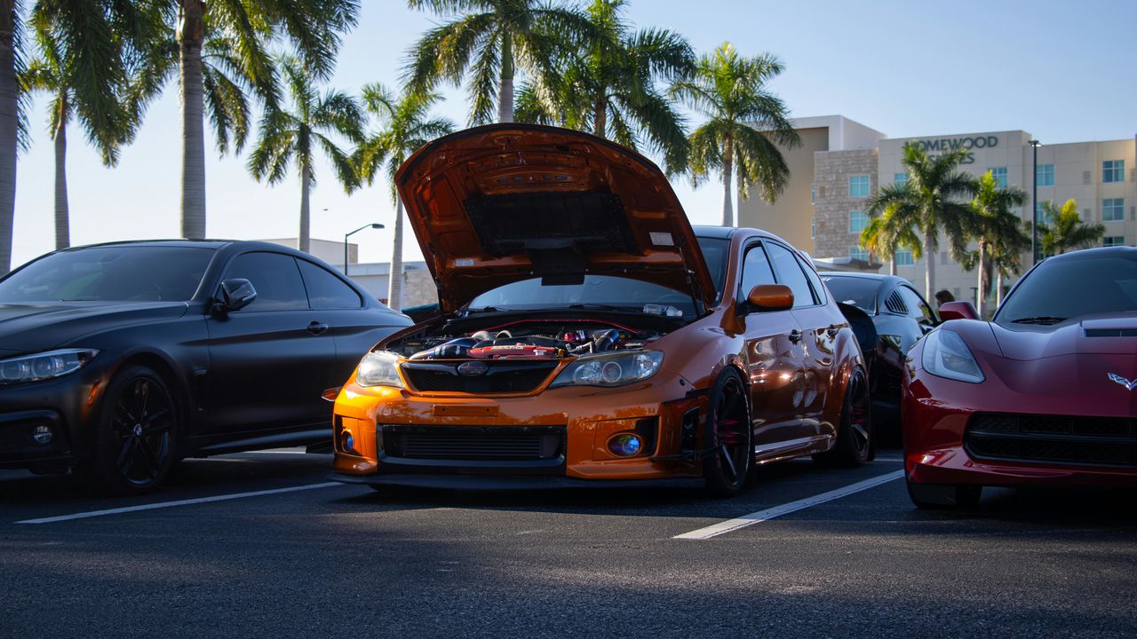 Помаранчевий тюнінгований автомобіль Subaru Impreza з відкритим капотом на парковці.