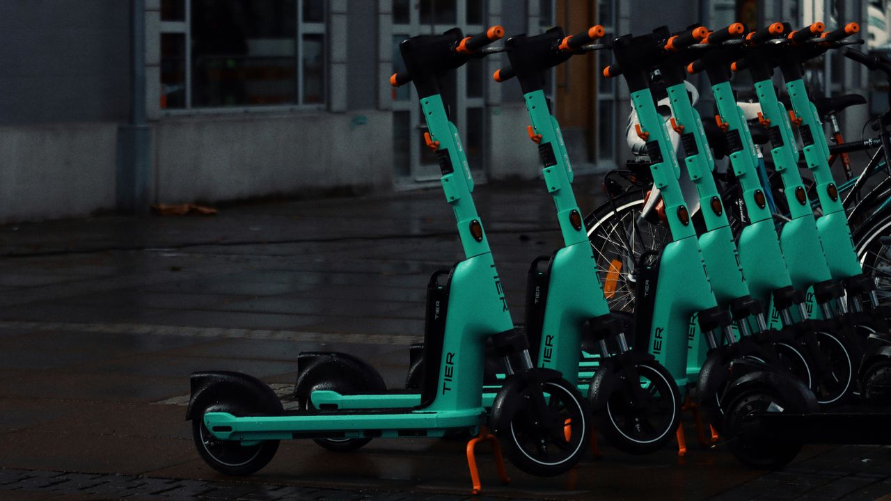 Ряд бірюзових електросамокатів для оренди на вулиці міста — популярний вид сучасної міської мобільності.